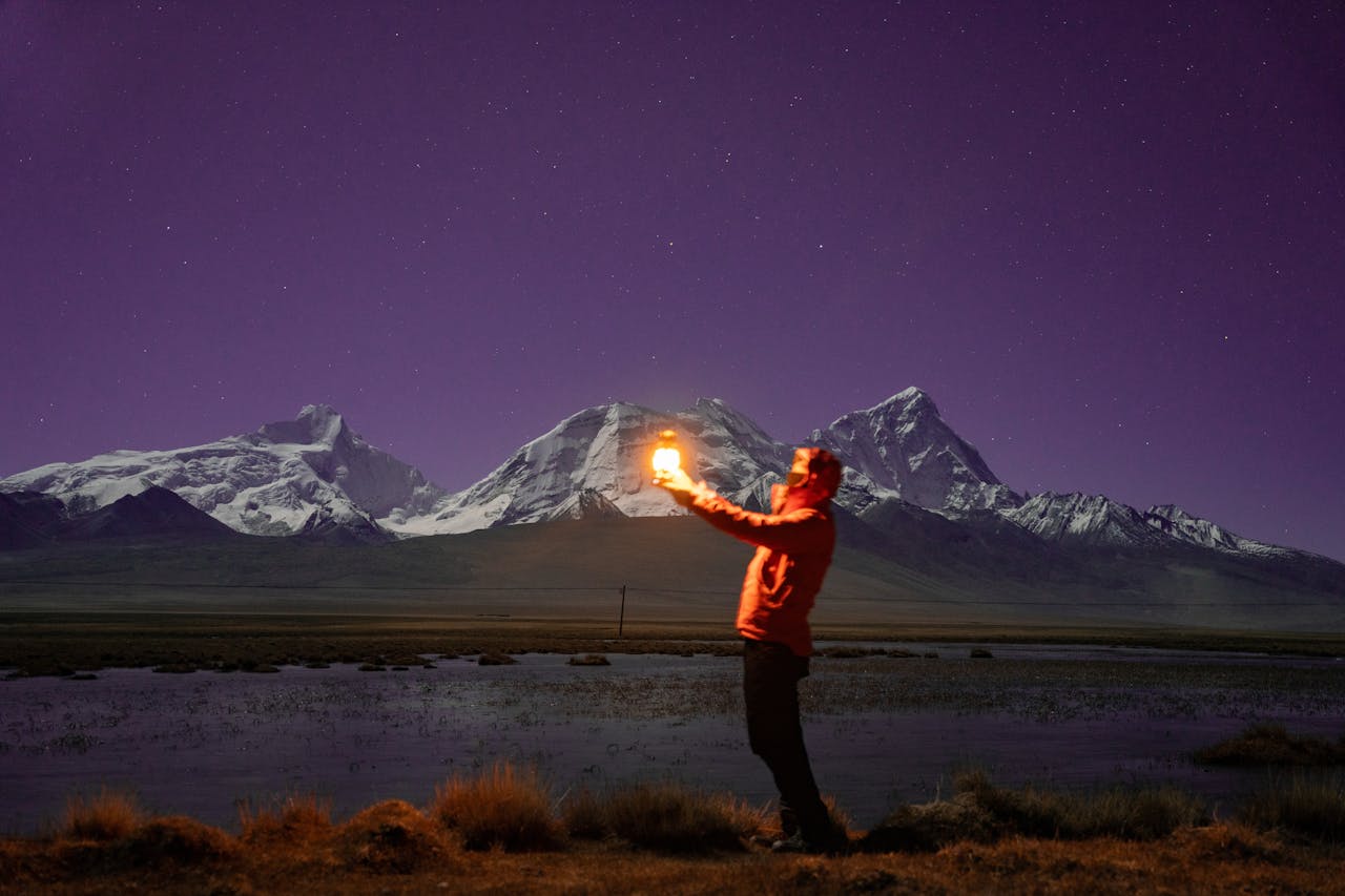services-02 Silhouette of a man holding a light with a majestic mountain backdrop at night.