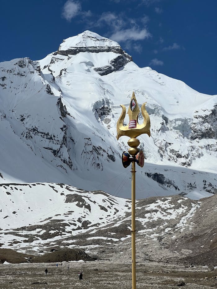 about-01 Gold trident in front of snow-covered peak under clear blue sky.