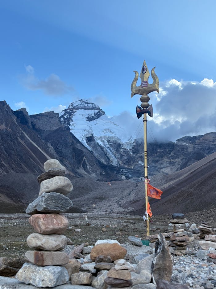 hero-img-01 Sacred trident symbol against the backdrop of a Himalayan peak with stone cairns in foreground.